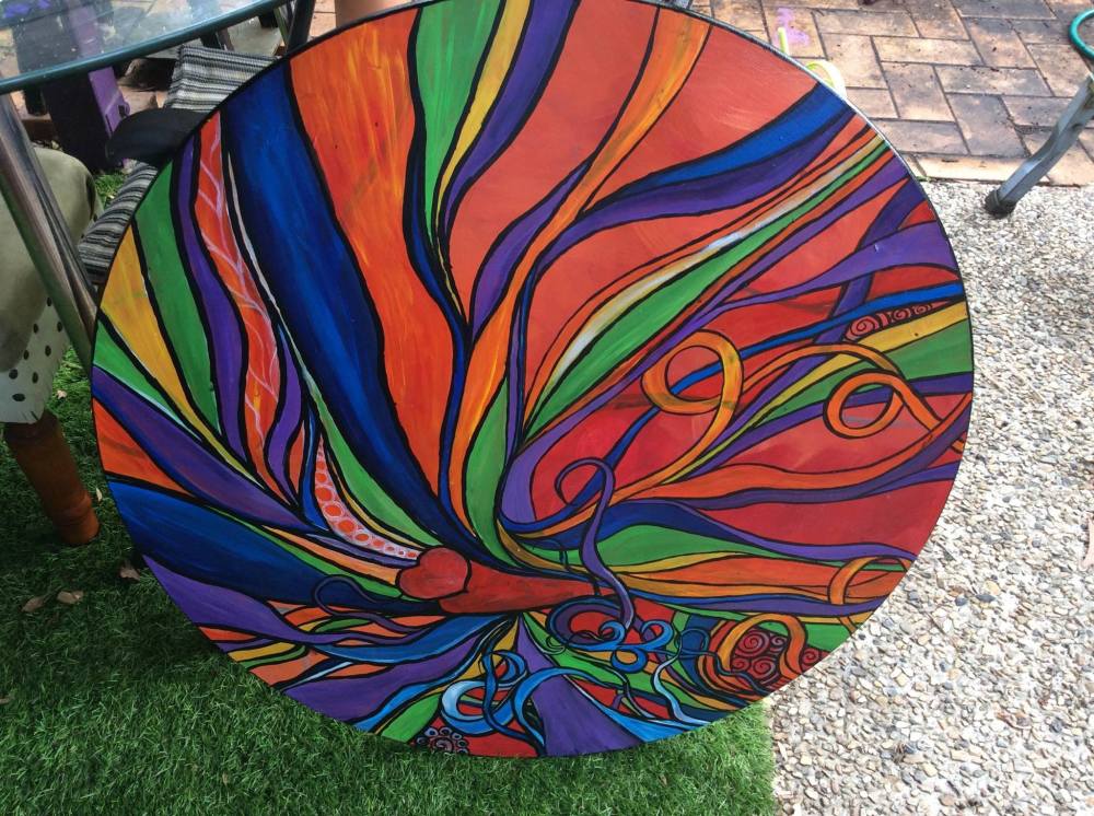 An abstract form of a butterfly in vivid rainbow colours painted by Sandy Skinner on a circular surface.